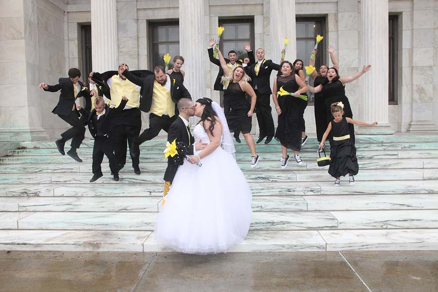 fun wedding photo of the bridal party jumping for joy behind the kissing bride and groom at the Toledo Museum of Art