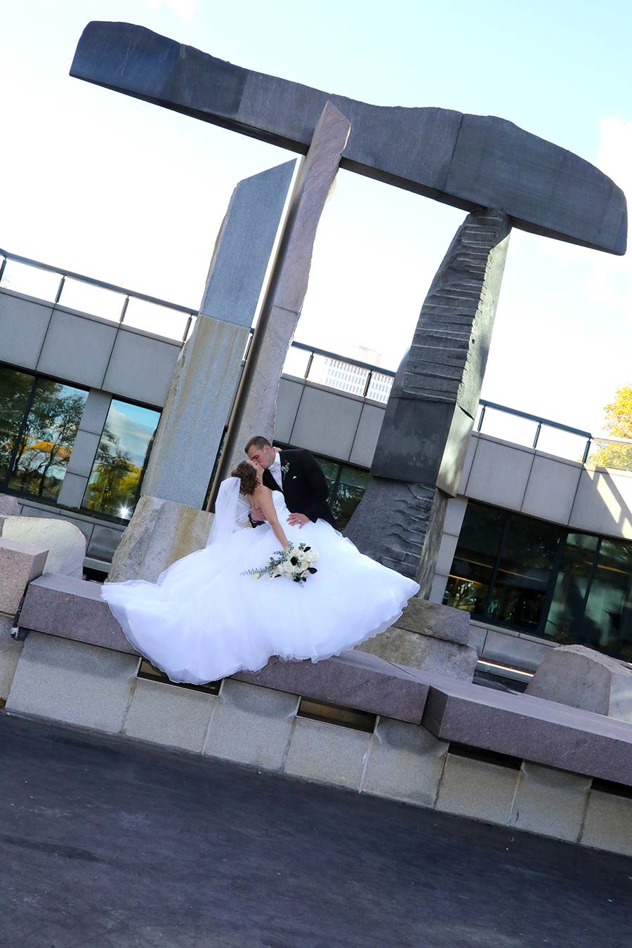 bride and groom kissing while under the arch rock sculpture at the reflecting pool in downtown Toledo behind the Renaissance Hotel on the Maumee River