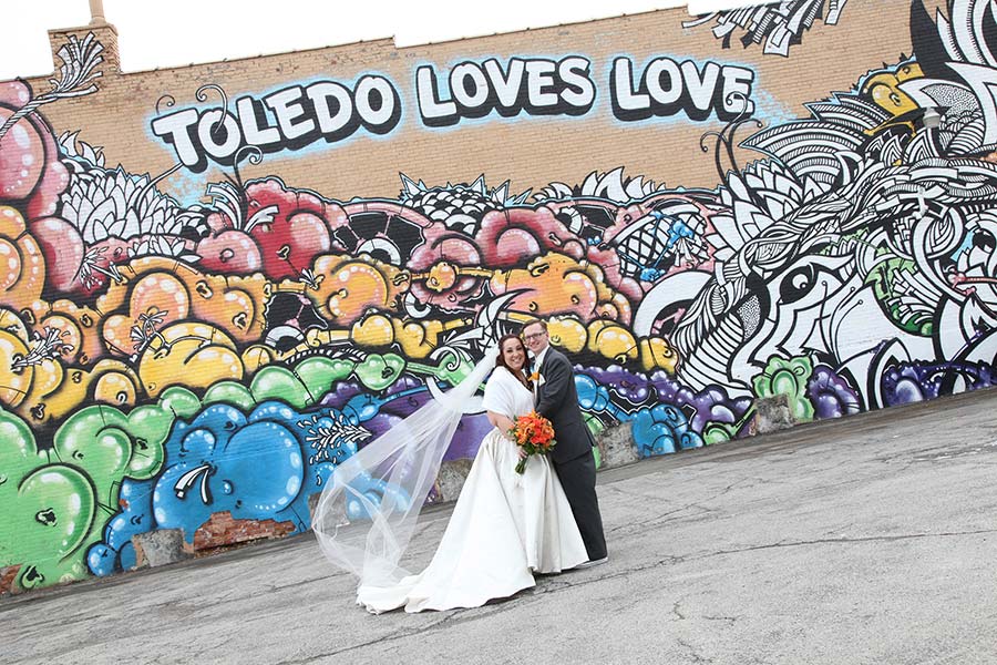 photo of the bride and groom holding her orange bouquet in front of the Toledo Loves Love mural in Uptown Toledo at Adams and 13th street