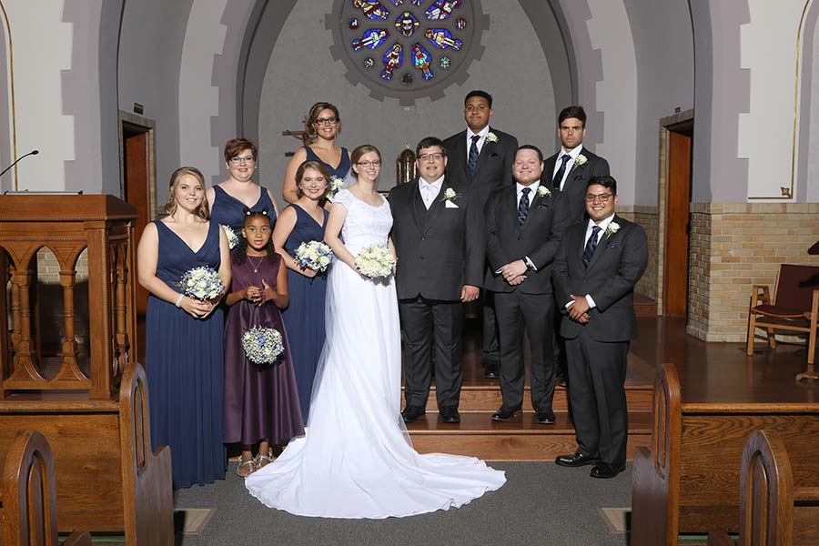 wedding portrait of the bridal party inside the Light of Christ Church in Blissfield, Michigan with the bridesmaids wearing long navy blue dresses