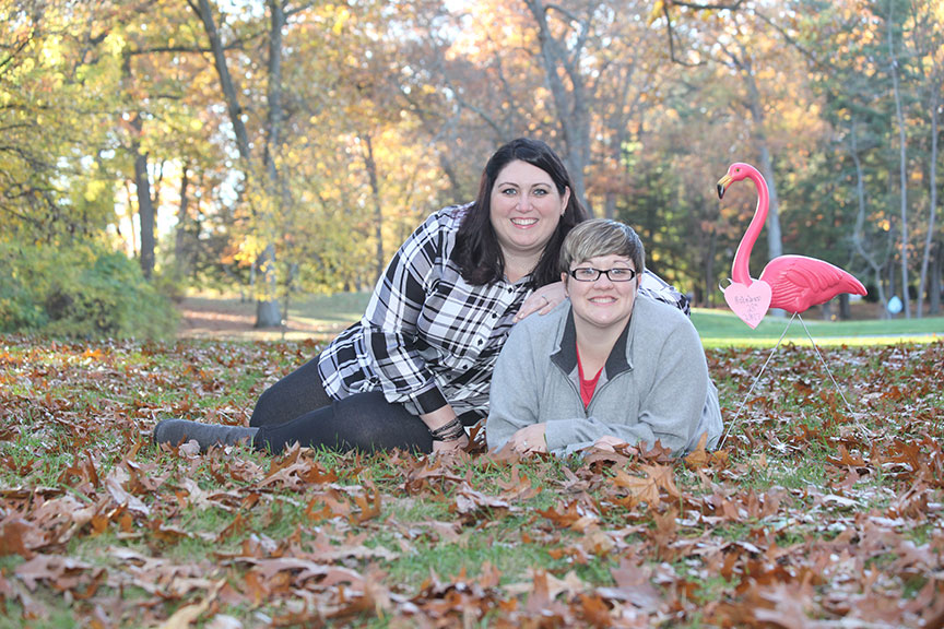 same sex couple engagement photo taken in the park in the fall with a pink flamingo in the background