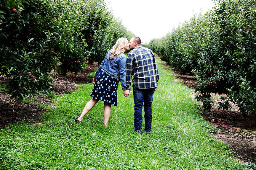 engaged couple stops for a kiss in between the rows of apple trees in Kreps Apple Orchard