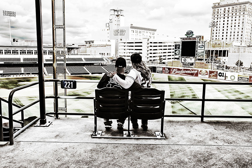 engaged couple wearing personalized jerseys sitting in the stadium chairs at the Toledo MudHens baseball park