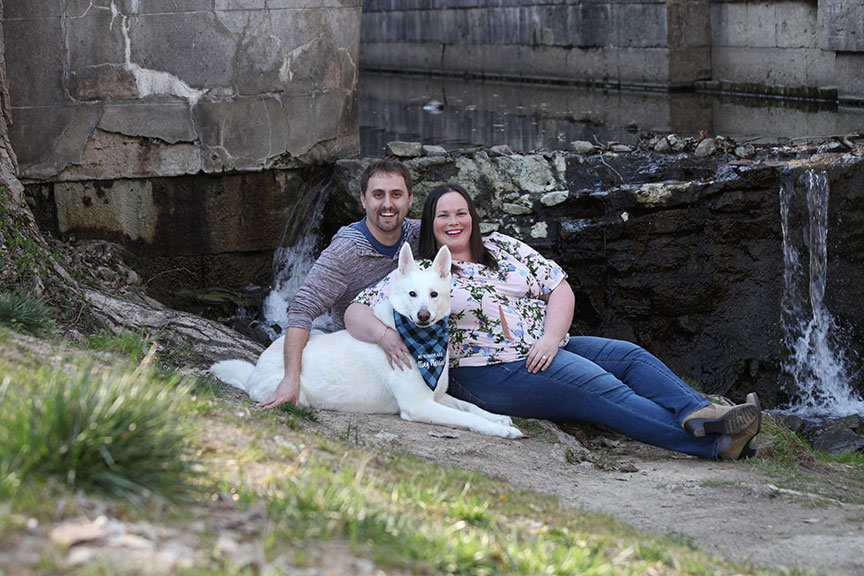 man and woman posing for their engagement pictures with their white dog near the waterfall at Side Cut Park in Maumee Ohio