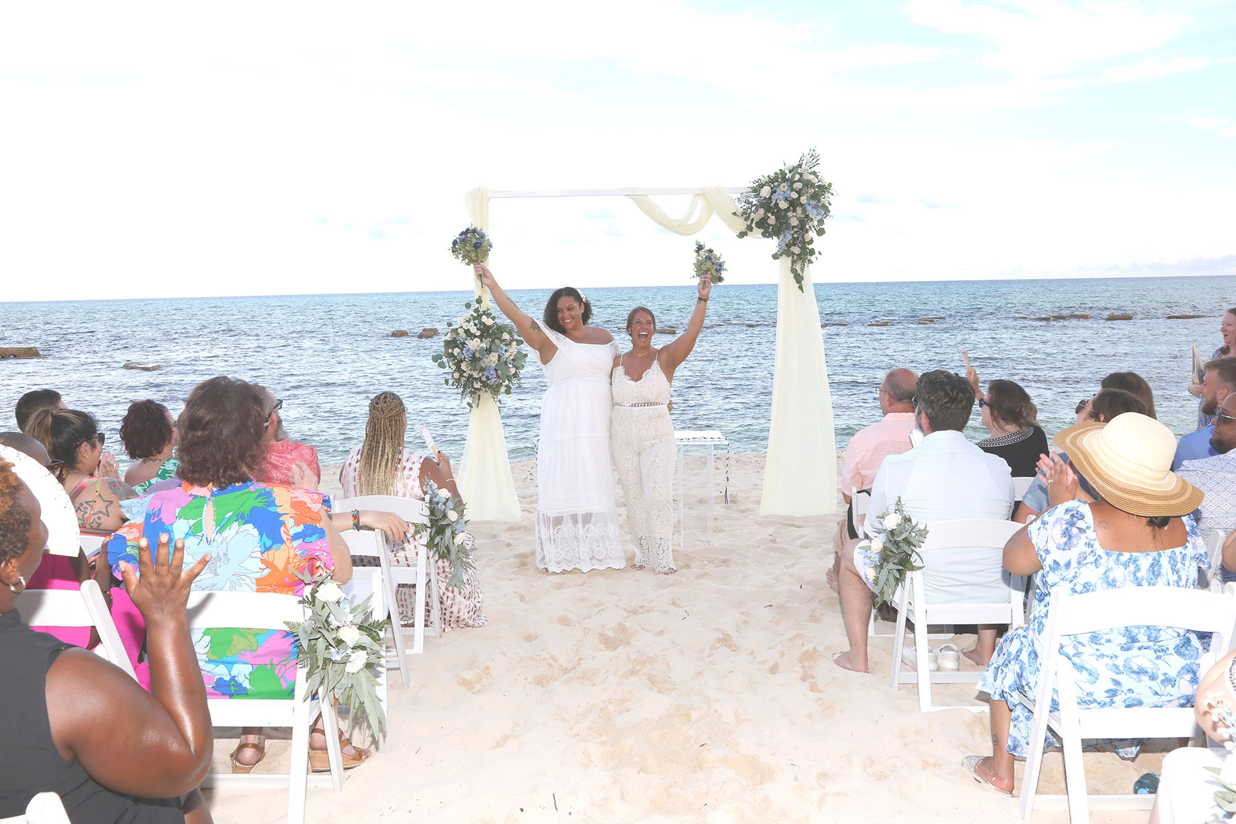  LGBTQ couple with their bouquets in the air after their beach wedding ceremony in Riviera Maya Mexico