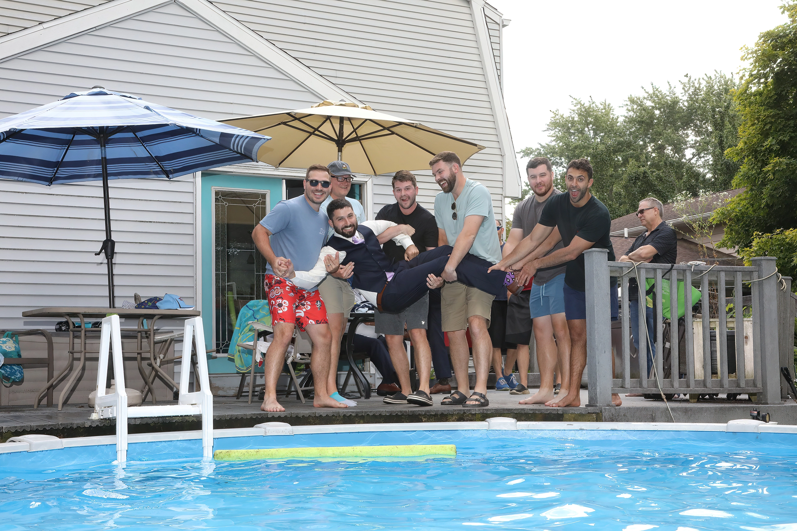 groomsmen having fun and attempting to throw the groom into the swimming pool before the wedding