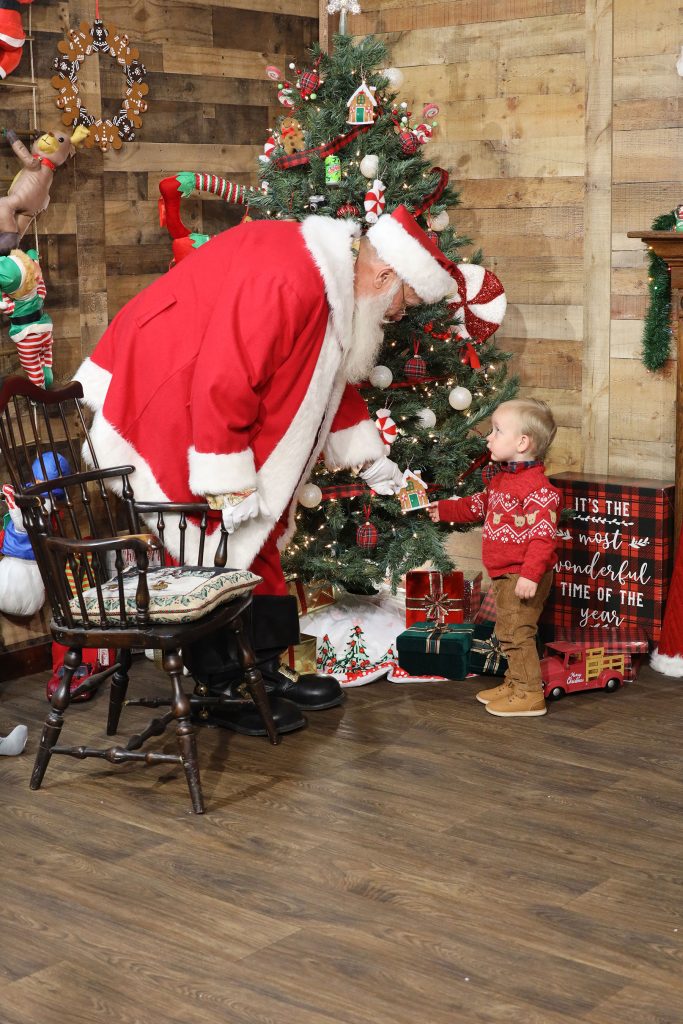 Santa talking to a two year old boy in front of a christmas tree inside Kurt Nielsen Photography