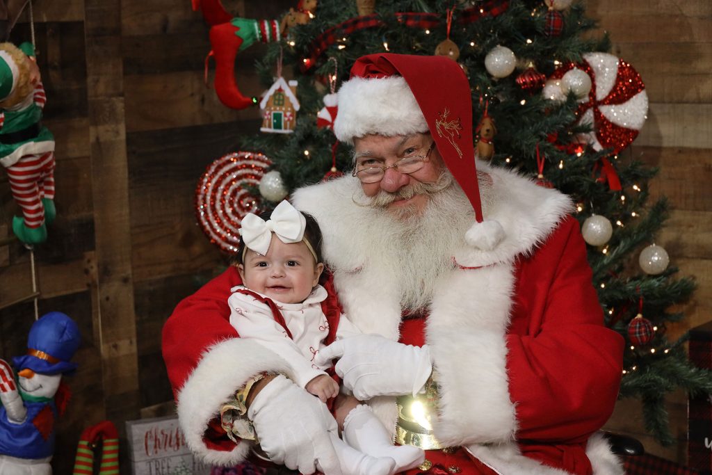 Santa holding a smiling 4 month old baby girl inside Kurt Nielsen Photography's Santa's workshop