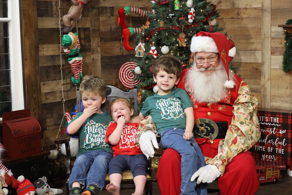3 small siblings sitting with Santa, two are crying