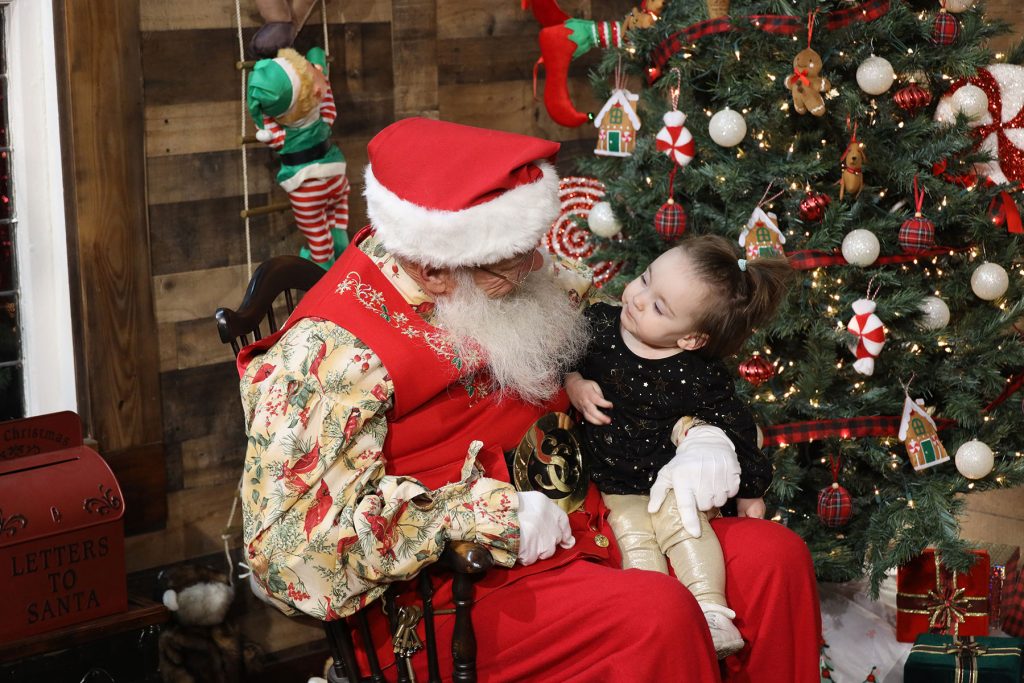 curious one year old baby girl sitting on Santa's lap looking up at him