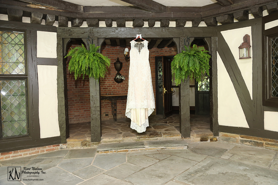 ivory Ashland wedding dress designed by Vatana Watters hanging between two ferns on the covered patio of the Club at Hillbrook