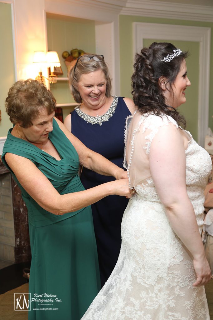the mom buttoning up the bride's dress