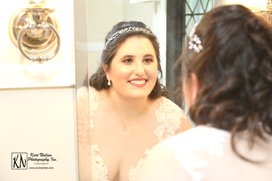 the smiling bride looking at her reflection in the mirror